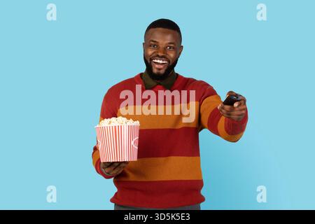 Concept de loisirs. Cheerfuk Black Young Man tenant Popcorn et télécommande Banque D'Images