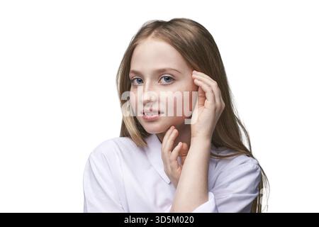 Jeune femme caucasienne avec de longs cheveux blonds en chemise blanche touchant le visage et souriant avec confiance Banque D'Images
