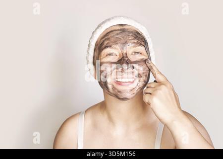 Jeune femme appliquant un masque noir. Produit pour le visage au charbon de bois. Acné et élimination de boutons. La thérapie au charbon de boue. Gommage dermatologique frais. Copyspace. Place f Banque D'Images