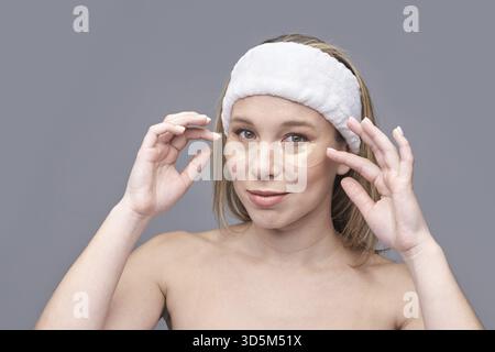 Jeune femme caucasienne appliquant sous les patchs oculaires pour la routine de soins de la peau avec expression détendue Banque D'Images