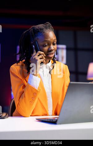 Femme freelance dans le bureau à domicile assis au bureau devant l'ordinateur portable, répondant à l'appel téléphonique. Travailleur à distance utilisant un ordinateur portable pour faire un travail en ligne, recevant un appel téléphonique sur smartphone Banque D'Images