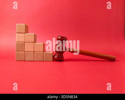 L'image montre un marteau en bois à côté d'une pile de cubes en bois sur un fond rouge. Banque D'Images