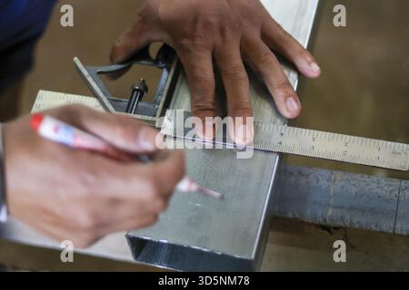 Gros plan de la main de travailleur qualifié avec la mesure de la concentration et le marquage du tube en acier. Utilisation de la règle carrée pour la précision dans l'atelier de fabrication du métal Banque D'Images