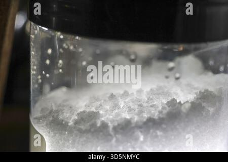 Vue macro fascinante de cristal de sel blanc se dissolvant dans l'eau transparente. la réaction chimique à l'intérieur du verre crée un nuage abstrait de particules an Banque D'Images