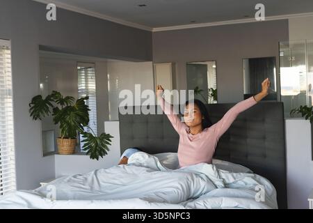 Couple diversifié se réveillant dans une chambre moderne avec literie blanche, plantes en pot et lumière naturelle Banque D'Images