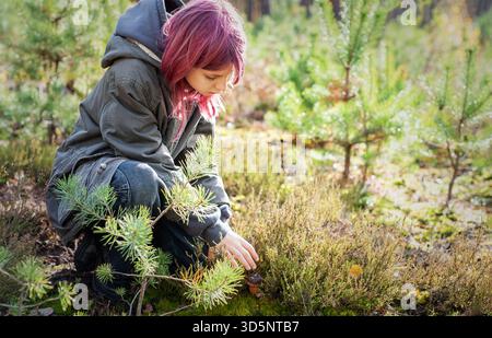 Enfant aux cheveux roses accroupi, découvrant un champignon dans une forêt Banque D'Images