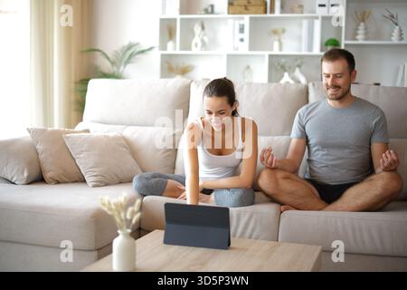 Couple préparant des cours de méditation de yoga en ligne sur tablette assis sur un canapé à la maison Banque D'Images
