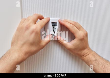 mains masculines de l'électricien installant l'interrupteur d'éclairage électrique à la maison. Remplacement. Banque D'Images