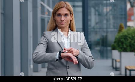 Sérieuse femme d'affaires adulte caucasienne ponctuelle pointant vers montre-bracelet regardant la femme d'affaires caméra vérifiant le portrait de l'heure dans la ville femme du centre-ville Banque D'Images