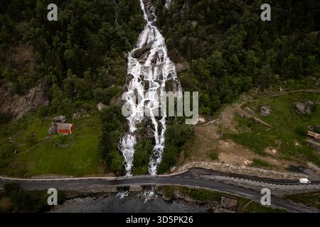 Vue aérienne de la cascade plonge sur le versant verdoyant de la montagne, contrastant avec la petite maison rouge nichée au milieu de la verdure luxuriante, O. Banque D'Images
