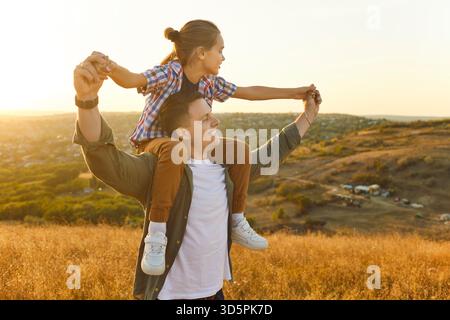 Heureux père et fils jouant au coucher du soleil ensemble, papa portant l'enfant sur les épaules Banque D'Images