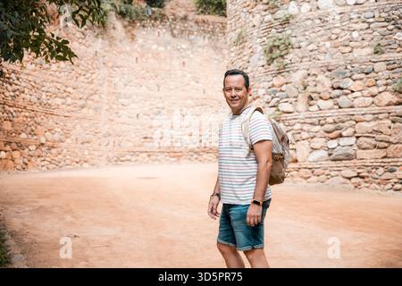 Homme avec sac à dos souriant à la caméra dans un cadre de pierre historique Banque D'Images