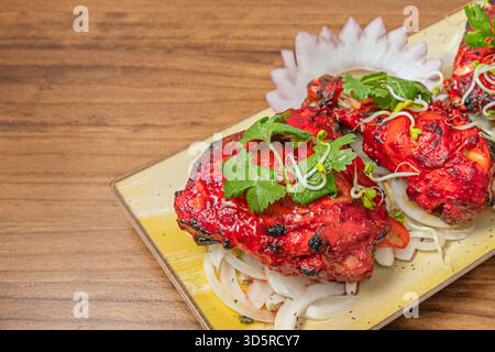 Un gros plan détaillé révèle la texture légèrement carbonisée et les herbes accrochées à la peau du poulet Tandoori fraîchement cuit. Banque D'Images
