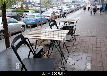 Des tables vides attendent un jour d'automne froid et nuageux à Kiev alors que les gens passent. Banque D'Images