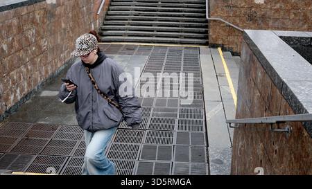 Une jeune femme descend les marches, concentrée sur son téléphone dans la ville pluvieuse de Kiev. Banque D'Images