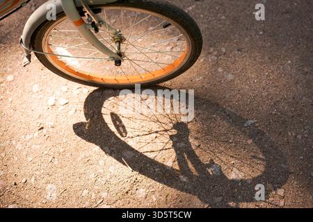 La roue de vélo roule le long d'une route asphaltée et jette de l'ombre, sur une journée ensoleillée d'été avec espace de copie. Mise au point sélective et gros plan || autorisation du modèle Banque D'Images