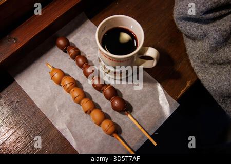 Würzburg, Allemagne, 23 décembre 2024. Brochettes recouvertes de chocolat à côté d'une boisson chaude sombre dans une tasse en céramique avec du vin chaud rouge sur la table du café à Banque D'Images
