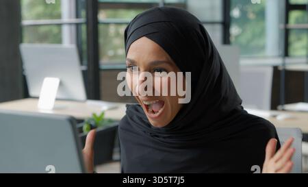 Heureuse femme d'affaires musulmane gagnant en disant wow au bureau avec la femme d'affaires islamique informatique dans le hijab femme employeur de fille travaillant gagner la victoire Banque D'Images