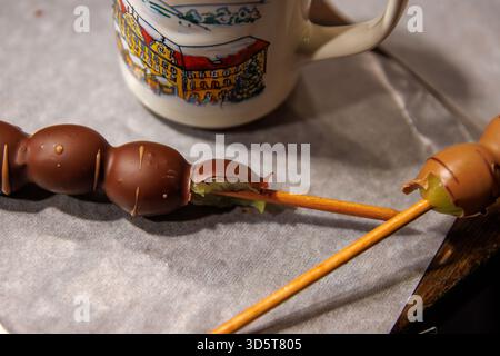 Würzburg, Allemagne, 23 décembre 2024. Gros plan de brochettes de raisin recouvertes de chocolat mordues avec des raisins verts frais à l'intérieur, posées sur du papier parchemin Banque D'Images