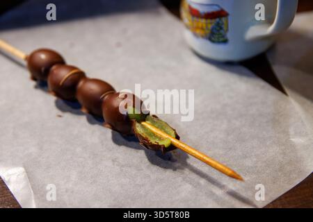 Würzburg, Allemagne, 23 décembre 2024. Gros plan de brochettes de raisin recouvertes de chocolat mordues avec des raisins verts frais à l'intérieur, posées sur du papier parchemin Banque D'Images