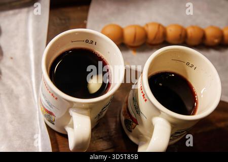 Würzburg, Allemagne, 23 décembre 2024. Deux tasses de vin chaud accompagnées de brochettes de fruits enrobées de chocolat sur papier parchemin lors d'un marché de noël. Haut v Banque D'Images