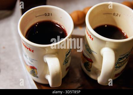 Würzburg, Allemagne, 23 décembre 2024. Deux tasses de vin chaud accompagnées de brochettes de fruits enrobées de chocolat sur papier parchemin lors d'un marché de noël. Haut v Banque D'Images
