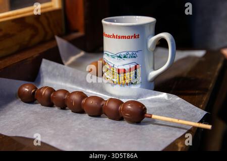 Würzburg, Allemagne, 23 décembre 2024. Brochettes recouvertes de chocolat à côté d'une boisson chaude sombre dans une tasse en céramique avec du vin chaud rouge sur la table du café à Banque D'Images