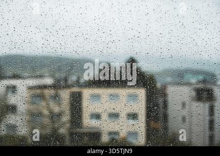 Des gouttes de pluie coulent le long d'une grande fenêtre de la maison. Gros plan, photo macro ultra grand angle, bâtiments en arrière-plan, personne Banque D'Images