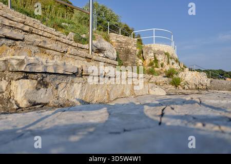 Marches en pierre construites dans la plage côtière rocheuse en Istrie, Croatie, avec des balustrades métalliques et de la verdure naturelle sous un ciel bleu clair d'été. Banque D'Images
