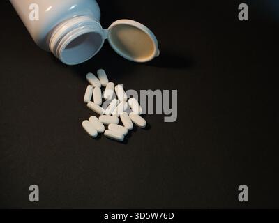 Pilules renversées de Open Medicine Bottle - Une dispersion de pilules ovales blanches, beaucoup marquées IH25, sont tombées d'une bouteille de médecine en plastique blanc ouvert o Banque D'Images