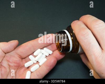 Main versant des pilules blanches de bouteille - gros plan des mains versant des pilules rectangulaires blanches d'une bouteille de médicament brune. Idéal pour la santé, le bien-être, dai Banque D'Images