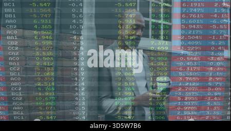 Homme debout portant une chemise noire blazer clair au mur de briques, tenant le téléphone avec les données du marché Banque D'Images