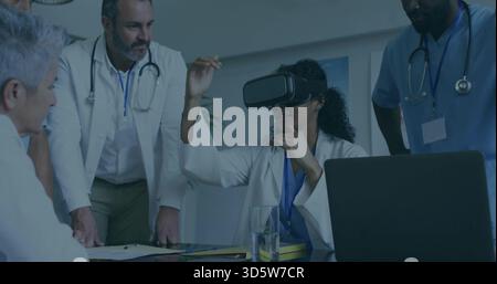 Clinicien interactif portant un casque VR gestuel à la table de la salle de réunion, ordinateur portable, blouses de laboratoire, gommages Banque D'Images