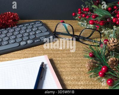 Station de travail festive Holiday - clavier moderne, lunettes et un ordinateur portable sur une surface dorée chatoyante avec des décorations rouges de vacances, suggérant festiv Banque D'Images