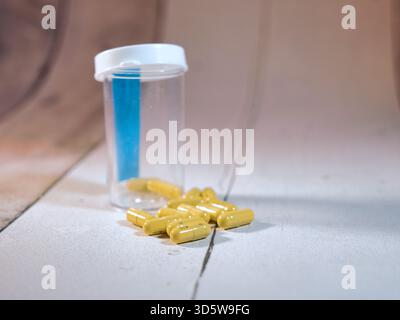Capsules jaunes renversées, bouteille de pilules - gros plan de pilules jaunes renversées à partir d'une bouteille d'ordonnance vide sur une surface blanche texturée, symboli Banque D'Images