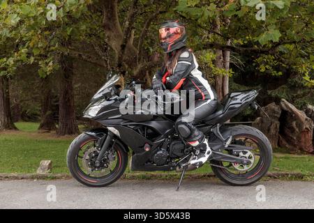 Cavalier en costume en cuir et casque assis sur un puissant sportbike noir dans la nature Banque D'Images