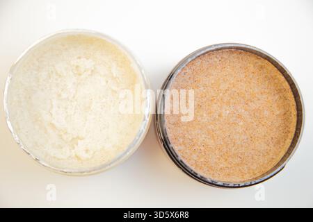 Pots de gommage corporel aux textures blanc crémeux et marron grossier, placés sur une surface propre Banque D'Images