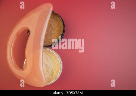 Deux pots de gommages corporels aux textures crémeuses et aux couleurs riches, positionnés sur un rose vif Banque D'Images