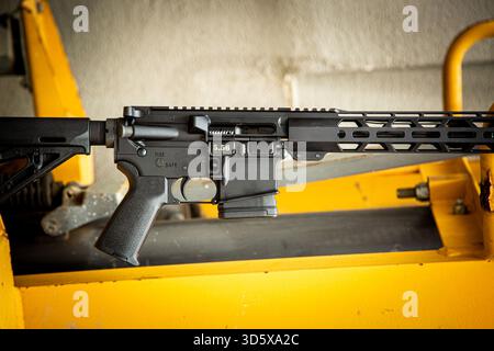 Fusil noir moderne de style AR-15 reposant horizontalement sur des machines industrielles jaune vif. Banque D'Images