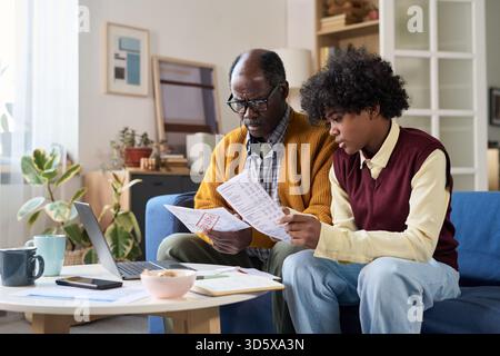 Homme noir mature et adolescent examinant les documents financiers ensemble Banque D'Images