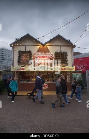 La maison Nutella et Churros Stand au marché de Noël Liverpool One, illuminés par des lumières festives au crépuscule avec les visiteurs qui passent devant. Banque D'Images