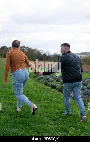 Un couple marche main dans la main à travers un champ verdoyant parsemé de lavande, trempant dans l'atmosphère automnale et partageant des moments joyeux ensemble sous Banque D'Images