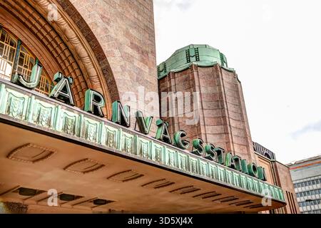 Façade avant de la gare centrale d'Helsinki avec son entrée voûtée, son horloge et ses figures emblématiques en pierre sous un ciel nuageux. Banque D'Images