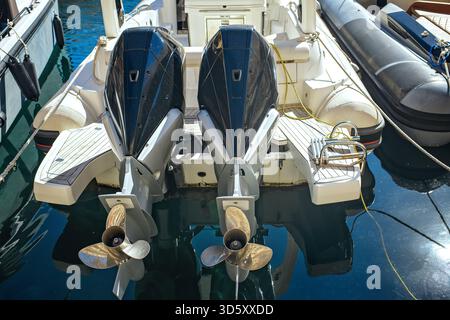 Gros plan de deux moteurs marins hors-bord sur un bateau à moteur moderne dans une marina, avec des détails de pont, des hélices et des reflets de l'eau par une journée ensoleillée. Banque D'Images