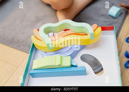 Ensemble de formes d'apprentissage en mousse multicolore placées à l'intérieur du plateau à jouets près de l'enfant sur le sol capturant le moment de jeu tactile, interaction créative Banque D'Images