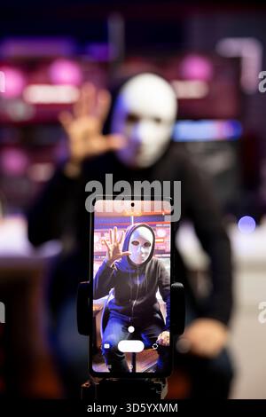 Gros plan du smartphone utilisé par le pirate dissimulant l'identité filmant la vidéo de rançon dans une base cachée. Focalisez la caméra du téléphone sur le trépied utilisé par le cybercriminel avec un masque pour enregistrer des séquences de chantage Banque D'Images