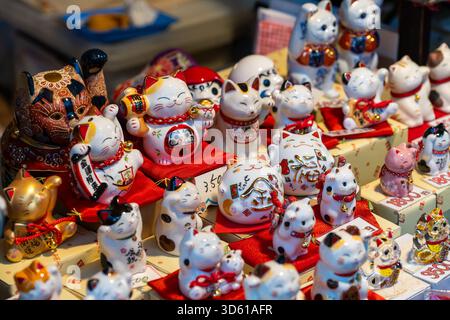 Une charmante exposition de figurines de chat agitant chanceux et d'autres charmes porte-bonheur en céramique à vendre dans une boutique de souvenirs dynamique à Kyoto Banque D'Images