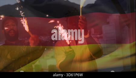 Tenant des étincelles, quatre amis dans des vêtements décontractés célébrant sur le balcon avec recouvrement de drapeau tricolore Banque D'Images