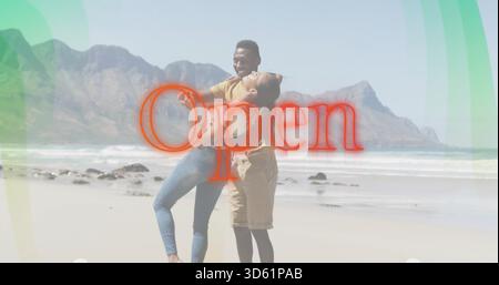 Tenant couple serrant sur la plage de sable, les deux portant des vêtements décontractés, recouvrement graphique ouvert rouge Banque D'Images