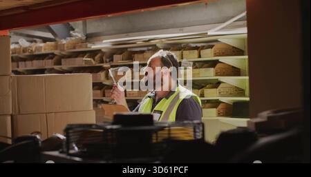 Inspection d'un homme portant un gilet haute visibilité, des lunettes de sécurité, vérification des boîtes étiquetées sur les portoirs avec une planchette à pince, un stylo Banque D'Images